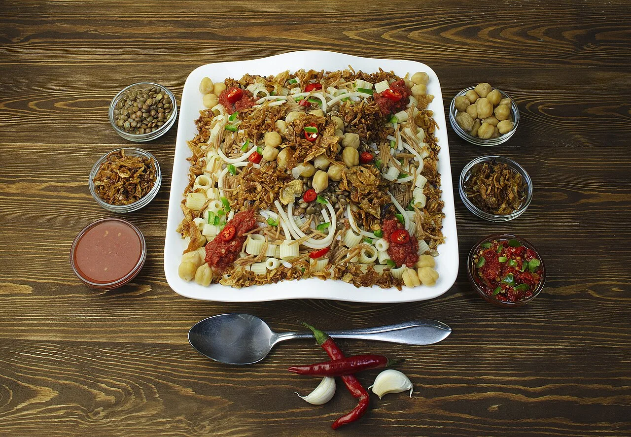 Египетская кошари с макаронами, бобовыми, жареным луком и соусами на столе.